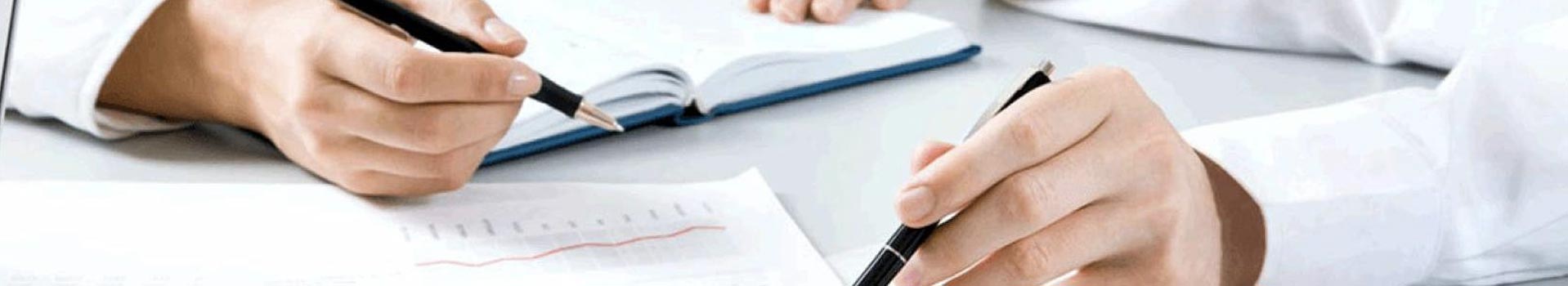 Two people's hands with pens, writing and pointing at a document and notebook
